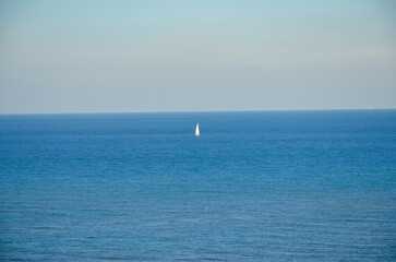 Fototapeta na wymiar A lonely sailboat on the horizon of the Mediterranean ocean