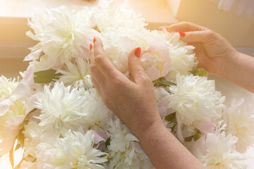 Female hands with bright red manicure on white peonies.