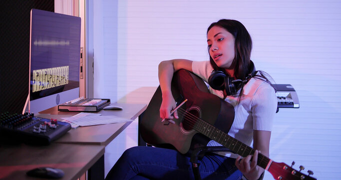 Young Asian woman holding guitar composing a song. Woman play acoustic guitar and think lyrics song. Woman songwriter, musician concept