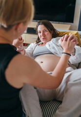 Young woman doula supporting pregnant female with a big belly in the home living room.  Woman's...