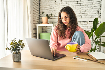 A young woman, focused and productive, working at her home desk with a laptop, sipping coffee, and feeling refreshed.