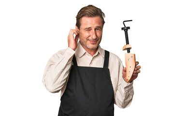 A middle-aged shoe maker covering ears with hands.