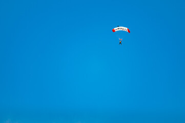 Parachutist with a white and red parachute against the blue sky