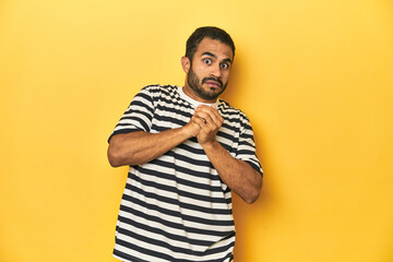 Casual young Latino man against a vibrant yellow studio background, scared and afraid.