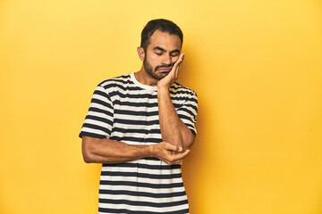 Casual young Latino man against a vibrant yellow studio background, who is bored, fatigued and need...