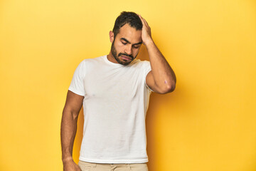 Fototapeta na wymiar Casual young Latino man against a vibrant yellow studio background, tired and very sleepy keeping hand on head.