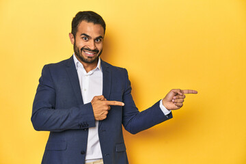 Professional young Latino man in business suit, yellow studio background, excited pointing with...