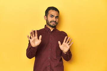 Casual young Latino man against a vibrant yellow studio background, rejecting someone showing a...