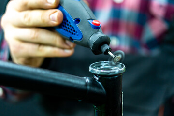 A bicycle mechanic has a grinding tool in his hands. The mechanic uses a drill to process the steering column of the highway frame. Bicycle repair.