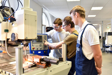 young apprentices in technical vocational training are taught by older trainers on a cnc lathes machine - 614875388