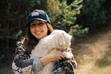 Woman walking with a white maltese dog on a forest path