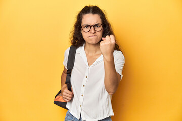 Caucasian university student with glasses, backpack, showing fist to camera, aggressive facial expression.