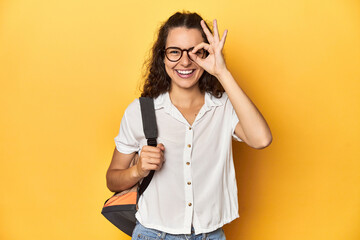 Caucasian university student with glasses, backpack, excited keeping ok gesture on eye.