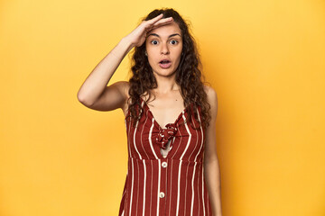 Young Caucasian woman, yellow studio background, shouts loud, keeps eyes opened and hands tense.