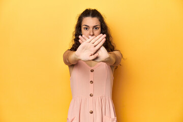 Young Caucasian woman, yellow studio background, doing a denial gesture