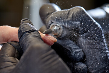 Manicure process in beauty salon, cleaning of nails by a milling cutter. Manicurist filing client's nails at table. Removing the nail plate with a milling machine. nail care concept