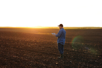 Smart farming technology and agriculture. Farmer uses digital tablet on field with plowed soil at sunset. Checking and control of soil quality, land readiness for sowing crops and planting vegetables
