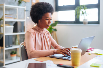 Fototapeta na wymiar Focused African-American businesswoman using laptop while sitting in office.