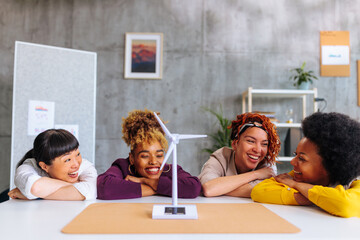 Four young multiracial business women gathered by model windmill celebrating successful project.