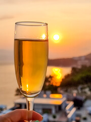 Caucasian woman hand holding champagne glass relax and enjoy luxury outdoor lifestyle in the ocean at sunset on summer beach holiday vacation trip.Backlit glass of water reflecting sunset