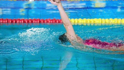 Female swimmer swimming in the indoor pool, training for competitive event backstroke. Concept of back crawl swimming style.