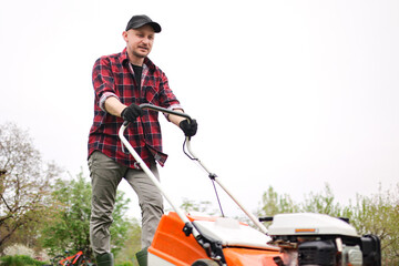 view of man in casual clothes mows lawn with lawn mower at backyard of his house. Husband takes care of garden on spring cloudy day. Modern gasoline garden equipment. Landscaping work