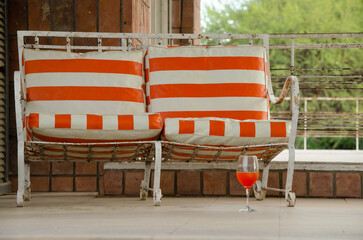 Iron armchair with.orange and white striped cushions, and a glass with orange drink on a vintage...
