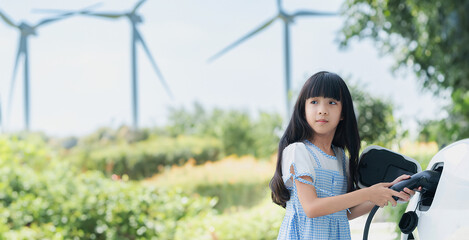 A playful girl holding an EV plug, a home charging station providing a sustainable power source for...