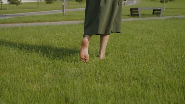 Walking girl with bare feet on a green lawn