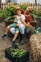 Young boy is sitting on his mother's lap in the garden.