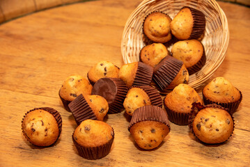 Delicious chocolate chip muffins falling from a wicker basket onto a wooden table.