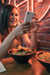 Vertical image of funny young girl chatting on her mobile phone while enjoying her poke bowl.