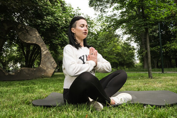 A young beautiful woman does yoga and meditates in the city park. The concept of sports and active life.