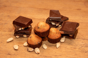 Close-up detail of pastries on a wooden table, delicious chocolate chip muffins surrounded by ounces of dark chocolate and almonds.