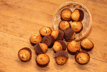 Close-up of many chocolate chip muffins falling from a wicker basket onto a wooden table.