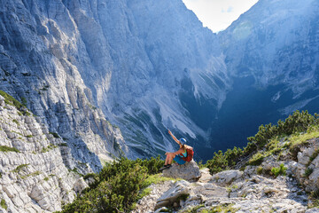 Fototapeta premium Impressive scale of mountains in Triglav National Park, Slovenia. Woman on via ferrata sits on a rock and points up, towards the top. Summer, adventure, active.
