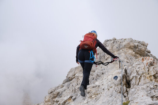 Active woman secured to via ferrata cable, advances on a route at Tofana di Mezzo, Dolomites, Italy, on a ridge surrounded by fog. Adventure, courage, europe, Summer, activity.