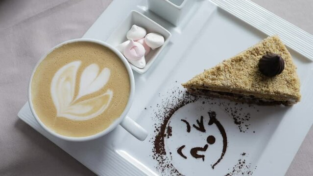 cappuccino foam in white cup on square plate, delicious cake on background, drawing painted with cocoa powder