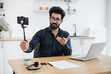Focus on modern cell phone placed in tripod being held by tired indian man in glasses sitting at...