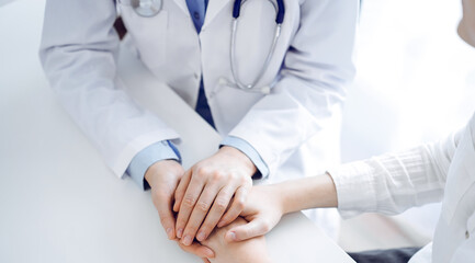 Doctor and patient sitting near each other at the table in clinic office. The focus is on female physician's hands reassuring woman, only hands, close up. Medicine concept