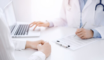 Doctor and patient discussing something and using laptop while sitting opposite each other at the desk in clinic office. Perfect medical service and medicine concept