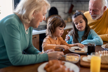 Senior woman and senior man having breakfast with two children at dinning table in the kitchen at home.