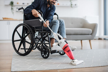 Cropped view of smiling man with mobility impairment handling debris on carpet with wireless...