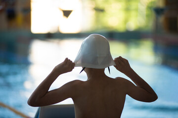 Silhouette of a swimmer boy who puts on a cap for swimming - 614897704