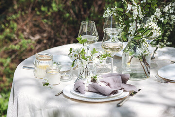 Rustic zero waste wedding decor with natural elements. Fresh spring blooming flowers, candles, linen napkins, wine glasses. Eco friendly decoration for the special holiday dinner. Romantic cozy place