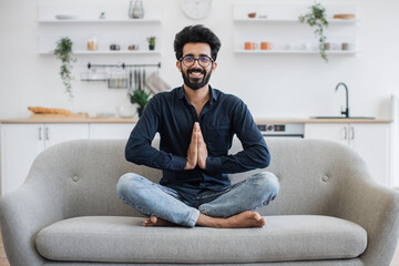 Young bearded man in jeans and dark shirt holding hands in anjali mudra while stretching in yoga...
