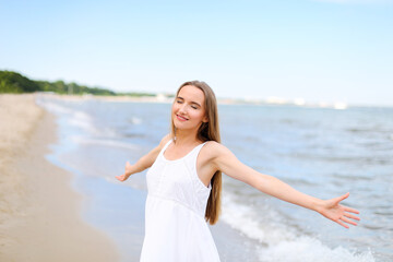 Fototapeta na wymiar Happy smiling woman in free happiness bliss on ocean beach standing with open hands. Portrait of a multicultural female model in white summer dress enjoying nature during travel holidays vacation