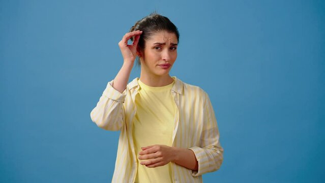 Young woman with bun examines skin of face in disappointment