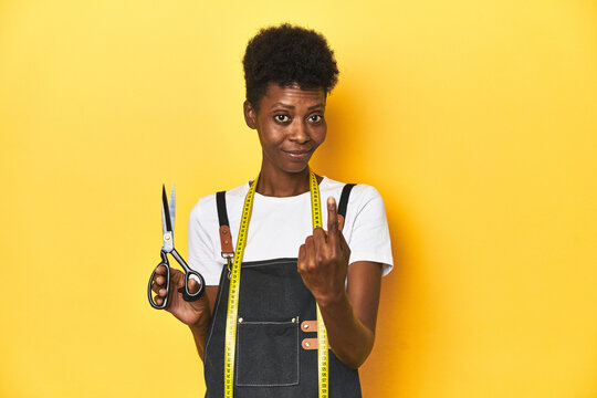 African tailor with scissors and measuring tape, fashion concept pointing with finger at you as if inviting come closer.