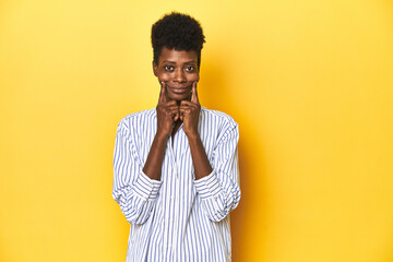 African businesswoman, blue striped shirt, yellow backdrop, doubting between two options.